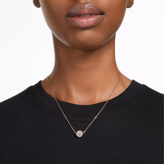 A person wears the Swarovski Una Angelic Necklace Pendant, elegantly crafted in a simple rose gold-tone and featuring a stunning pendant. Set against a plain black shirt, the image beautifully captures the neck and upper chest area, drawing attention to this exquisite piece from Swarovski.