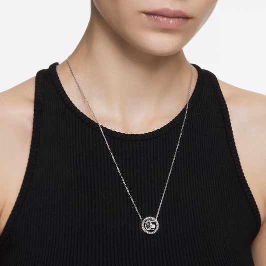 A person is shown from the shoulders up wearing a black sleeveless top. They have on a Swarovski Dextera Necklace Pendant, featuring a circular design with delicate crystal pavé. The background is plain white.