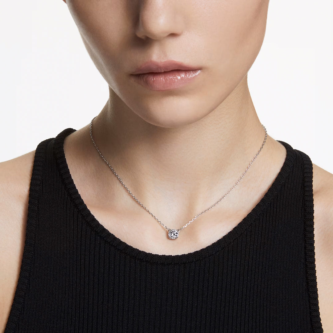 The individual is adorned with a Swarovski Stilla Necklace Pendant on a sleek silver chain. The rhodium-plated necklace shimmers against their black sleeveless top, while the neutral backdrop accentuates its beauty.