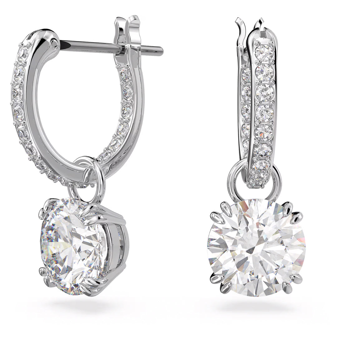 Close-up of the Swarovski Stilla Drop Earrings by Swarovski, featuring two silver drop earrings adorned with small crystals and rhodium plating. Each earring showcases a large round diamond pendant at the center, with intricate, sparkling details beautifully highlighted against a white background.