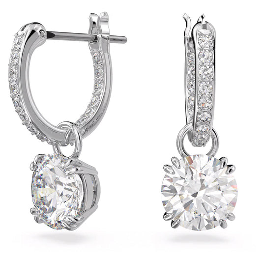 Close-up of the Swarovski Stilla Drop Earrings by Swarovski, featuring two silver drop earrings adorned with small crystals and rhodium plating. Each earring showcases a large round diamond pendant at the center, with intricate, sparkling details beautifully highlighted against a white background.