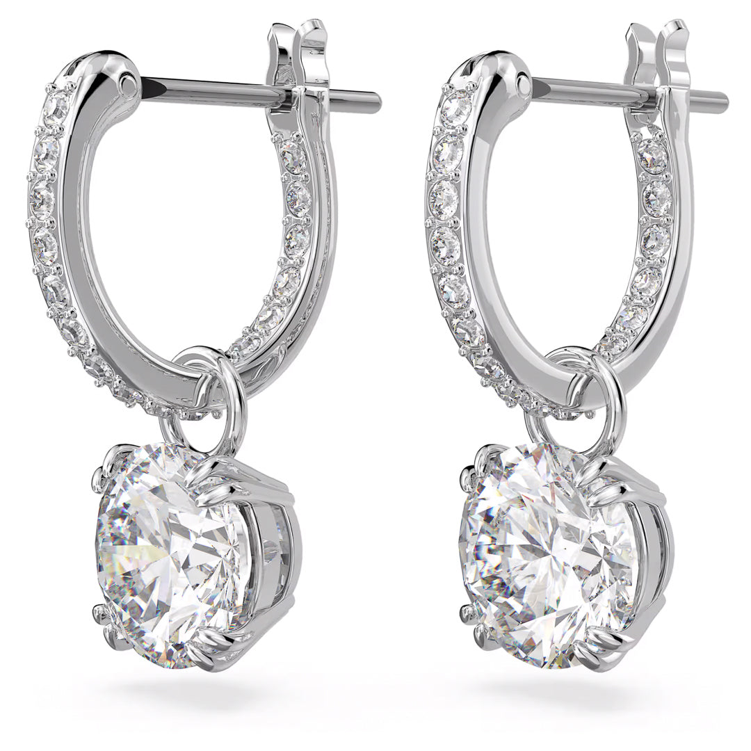 The Swarovski Stilla Drop Earrings by Swarovski are exquisitely designed with rhodium plating, showcasing a row of small sparkling crystals along the top curve, and featuring a large center stone that gracefully dangles from each elegant silver hoop.