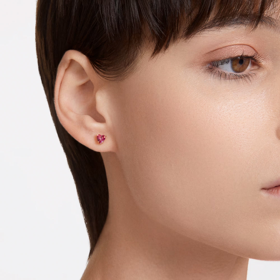 Close-up of a person with short brown hair wearing a Swarovski Chroma Stud Earring on the left ear. The fair skin tone highlights the gold-tone plated detail of this exquisite earring by Swarovski, featuring a small, heart-shaped zirconia design.