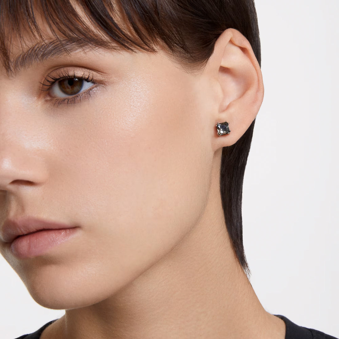 Close-up of a person with short hair, wearing a single Swarovski Millenia Stud Earring in black with subtle ruthenium plating on their left ear. They have smooth skin and are looking slightly away from the camera, maintaining a neutral expression.