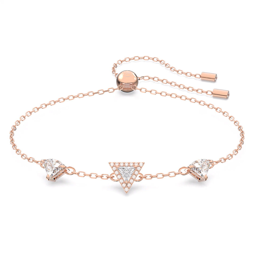 The Swarovski Stilla Bracelet by Swarovski is a rose gold-tone adjustable bracelet featuring a triangle-cut crystal charm adorned with small crystals, flanked by two heart-shaped Swarovski crystals on either side.