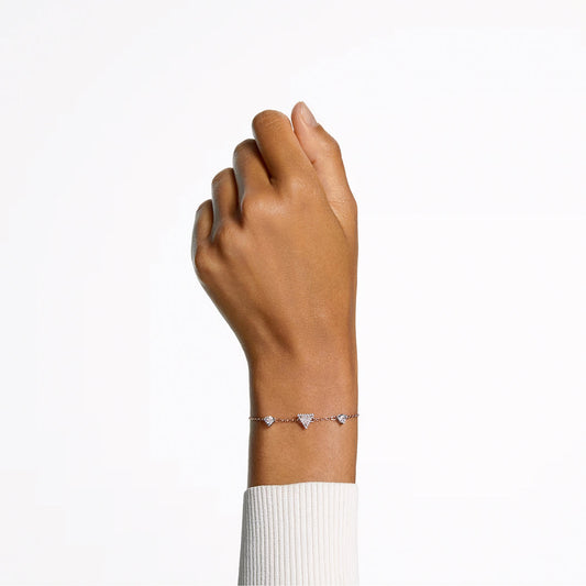 A hand wearing a light-colored sweater displays the exquisite Swarovski Stilla Bracelet, featuring a rose gold-tone design with delicate connected triangles, evoking the elegance of a triangle-cut crystal, against a plain white background.