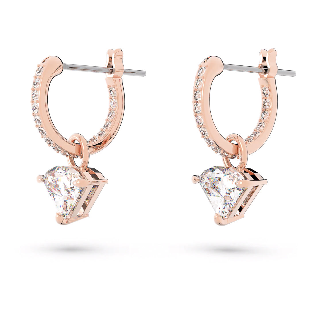 The Swarovski Stilla Drop Earrings showcase rose gold-tone hoops embellished with small, sparkling stones. Each earring boasts a dangling, triangle-cut crystal charm below the hoop, beautifully set against a plain white background to capture the elegance of Swarovski jewelry.