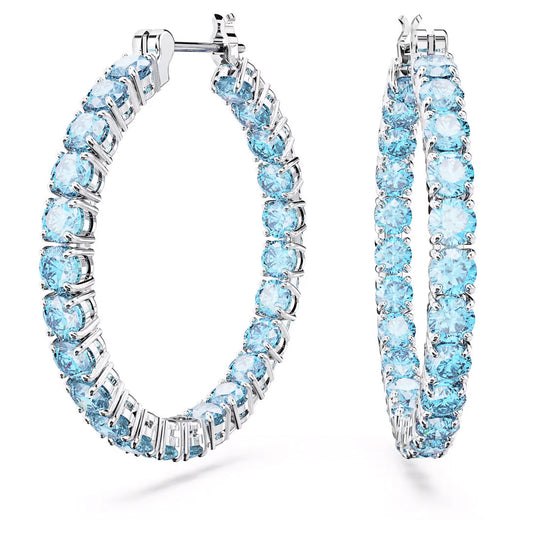 The Swarovski Matrix Hoop Earrings, rhodium-plated for enhanced shine, boast blue stones encircling their design. Displayed elegantly against a white background, these earrings exemplify sophistication.