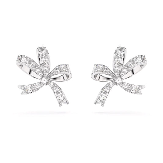 The Swarovski Hyperbola Stud Earrings by Swarovski are rhodium-plated and feature a bow-shaped design adorned with sparkling diamonds. These earrings reflect light beautifully, creating a shimmering effect, and include intricate ribbon-like loops and tails that highlight elegance and sophistication.