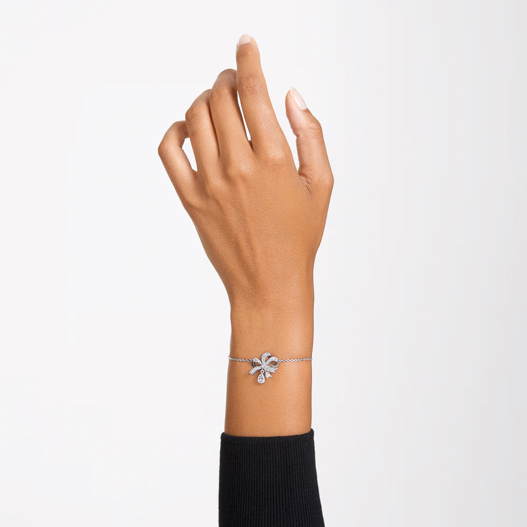 A hand adorned with a Swarovski Hyperbola Bracelet, exquisitely crafted using the chattonage technique and showcasing elegant leaf-like details, is raised against a plain, light background.