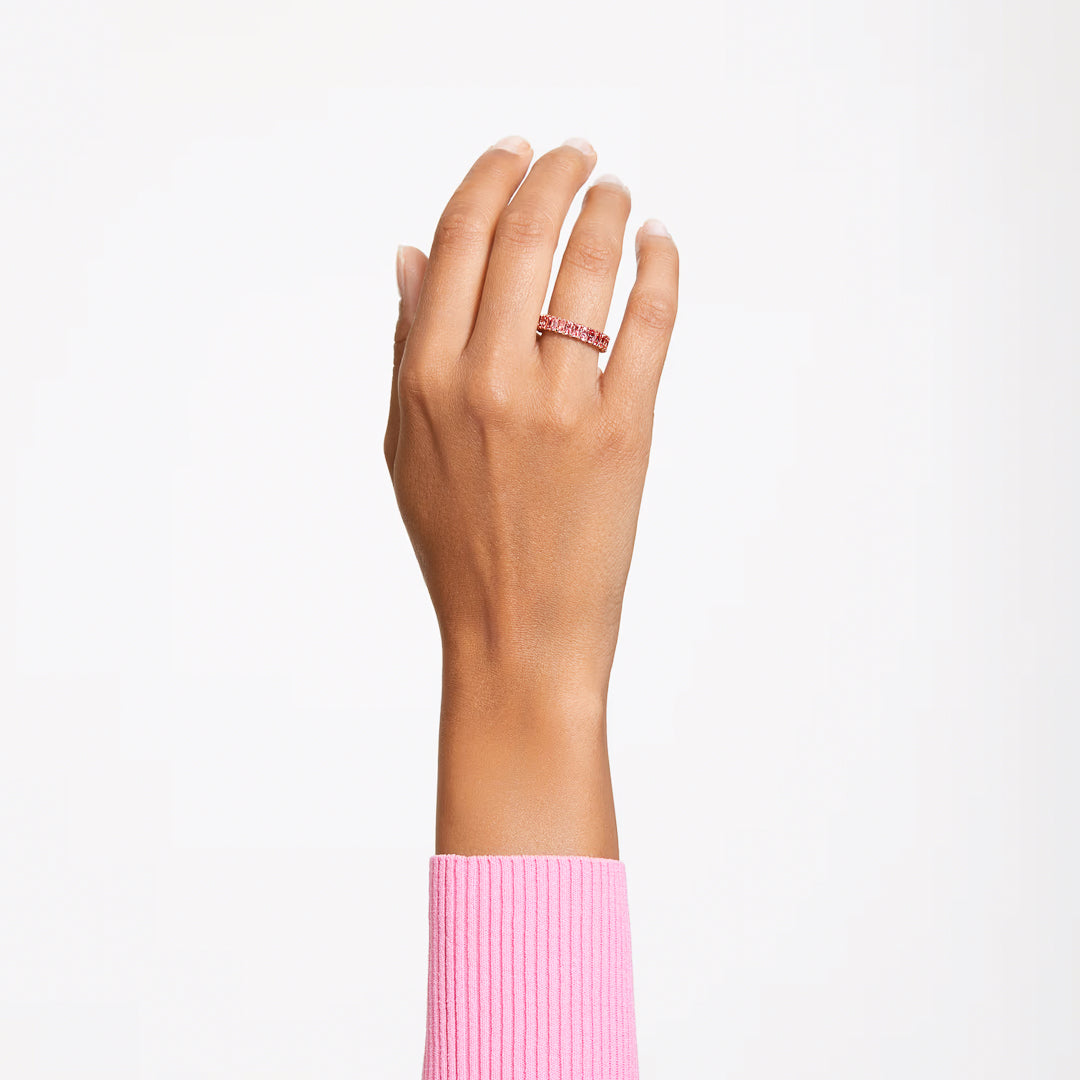 A hand clad in a pink sweater is held up against a plain white backdrop, showcasing the Swarovski Matrix Baguette Ring set with pink stones on the ring finger.