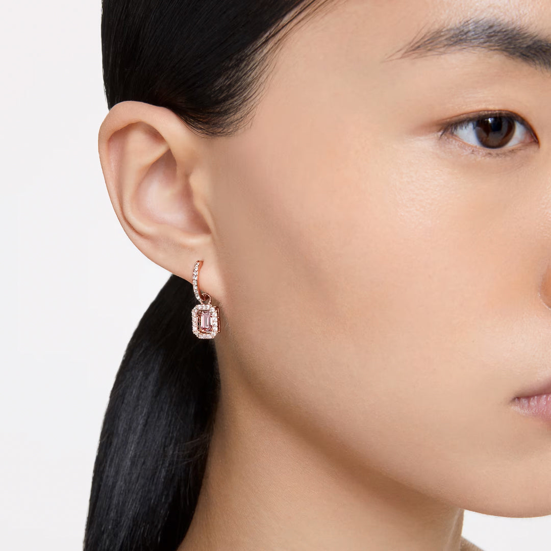 Close-up of a person wearing Swarovski Una Drop Earrings. The rose gold-tone and geometric design beautifully accentuate the earring against the person's smooth skin and hair pulled back.