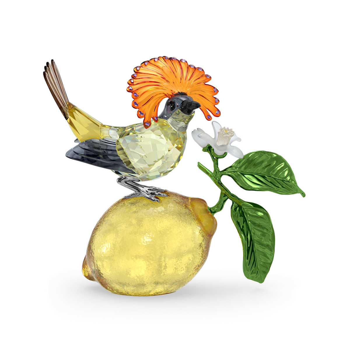 The Swarovski Idyllia Royal Flycatcher by Swarovski features a crystal figurine of a Royal Flycatcher with an orange crest, perched on a yellow lemon adorned with green leaves and a white flower, all beautifully crafted from Swarovski crystals and presented against a plain white background.
