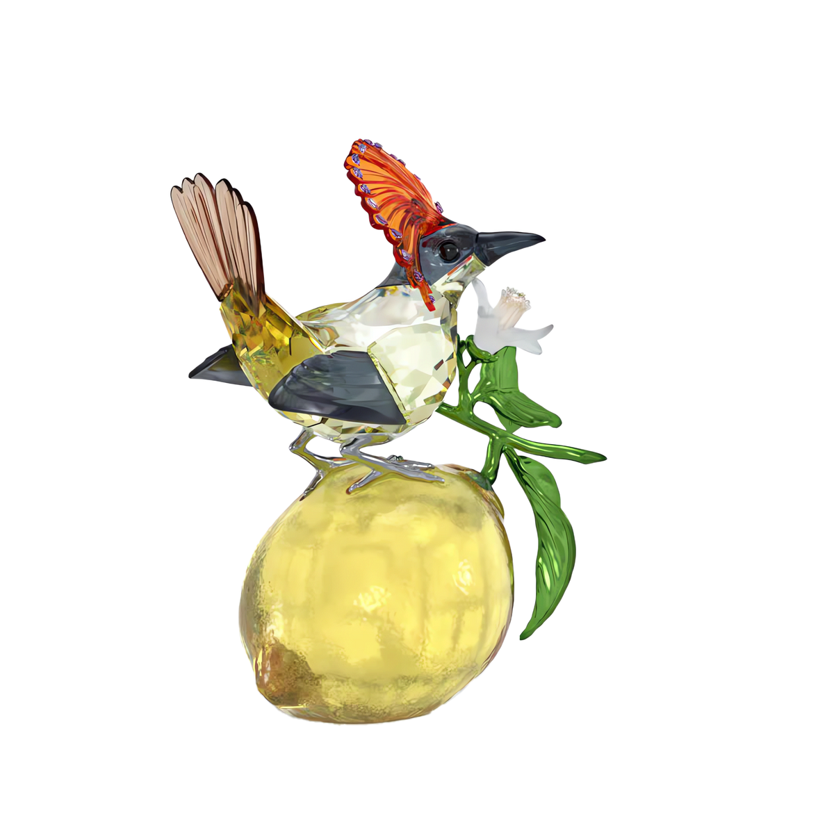 The Swarovski Idyllia Royal Flycatcher, a vibrant glass bird inspired by the Royal Flycatcher and featuring its signature red crest, is perched on a yellow glass lemon while holding a white flower in its beak. Green glass leaves accent the lemon, all set against a white background.