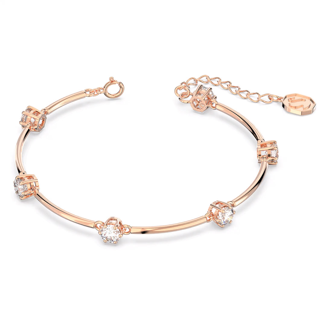 The elegant Swarovski Constella Bangle by Swarovski is crafted in a rose gold-tone, showcasing a slender band enhanced with small, round crystal zirconia accents arranged evenly. It features an adjustable chain and a clasp closure, finished with a petite hexagonal charm at one end.
