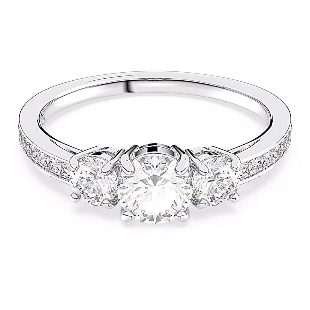 The Swarovski Attract Ring by Swarovski features a dazzling three-stone design with a central round diamond complemented by two smaller round diamonds, all set in a polished white gold band with a silver-tone finish. The band is embellished with smaller Swarovski Zirconia along its sides, offering an extra touch of elegance.