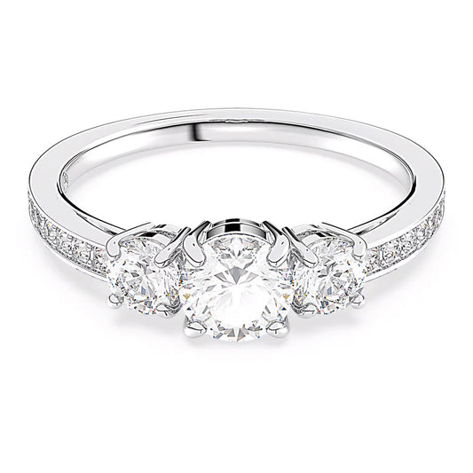 The Swarovski Attract Ring by Swarovski features a dazzling three-stone design with a central round diamond complemented by two smaller round diamonds, all set in a polished white gold band with a silver-tone finish. The band is embellished with smaller Swarovski Zirconia along its sides, offering an extra touch of elegance.