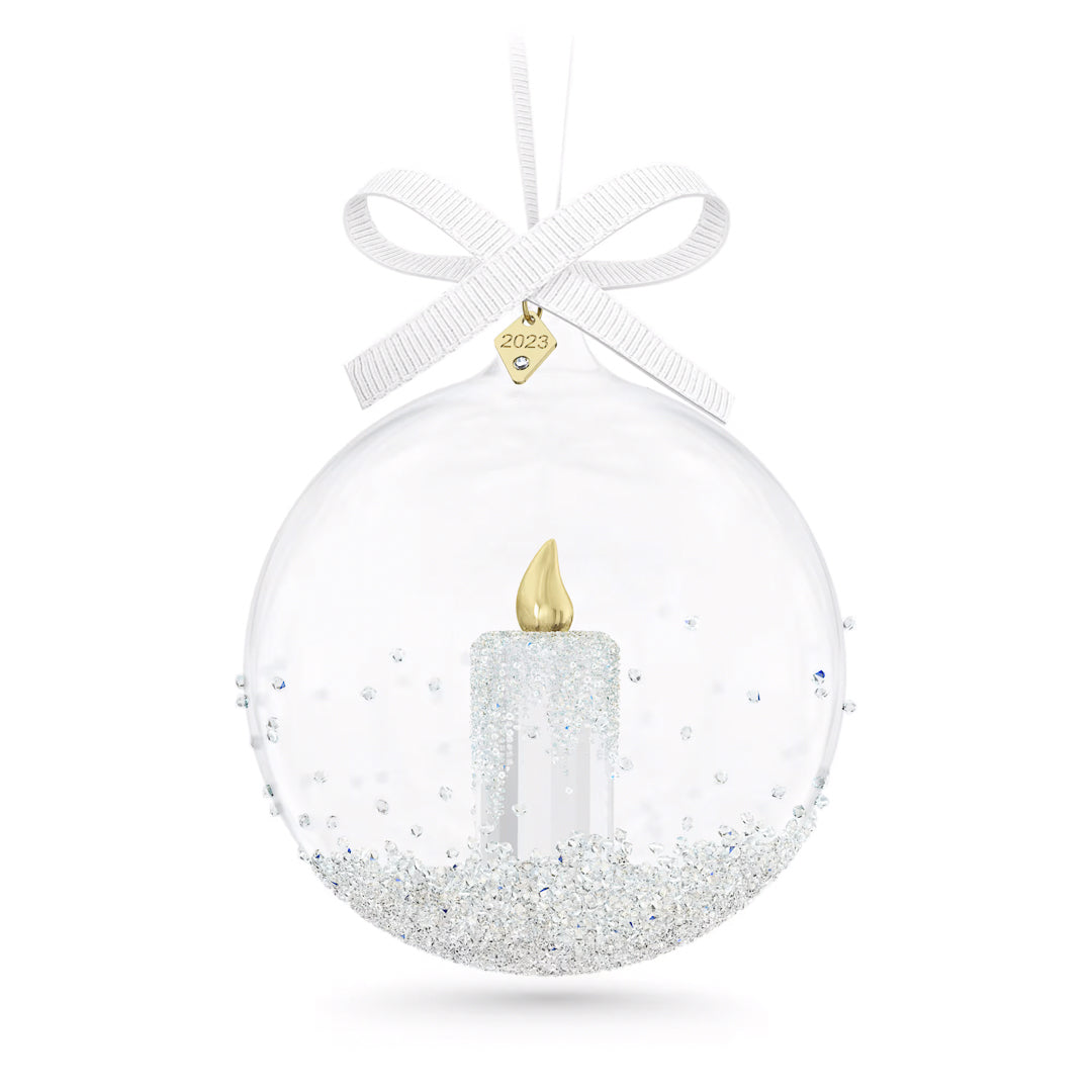 The Swarovski Annual Edition Ball Ornament 2023 Home Décor captures elegance with its clear design that includes a crystal candle motif accented with glitter and a miniature golden candle inside. Finished with a white bow and adorned with a gold tag labeled "2023," this ornament embodies the refined style of the Swarovski collection.