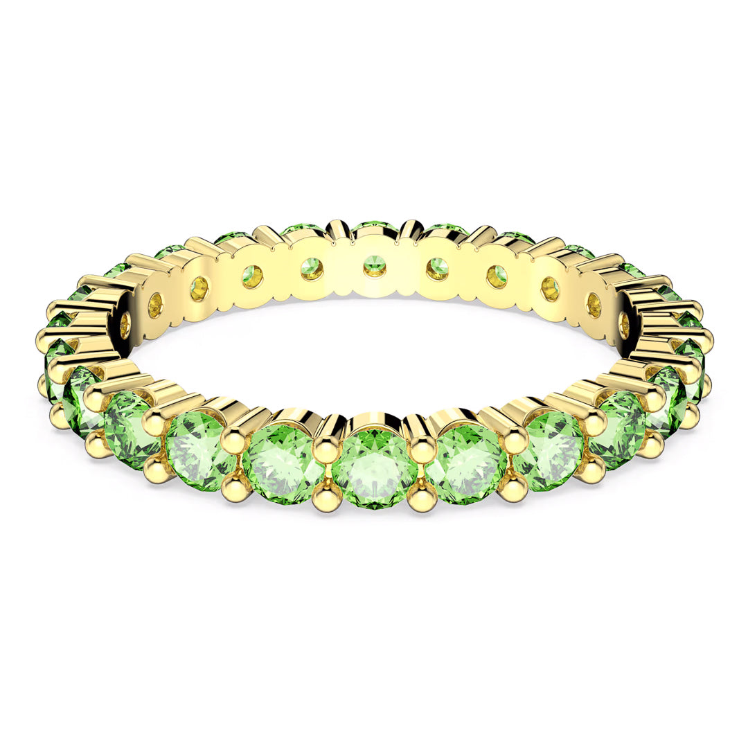 The Swarovski Matrix Ring by Swarovski is a gold-tone plated eternity band adorned with round green stones symmetrically arranged around it. The prong setting of the gems enhances the ring's delicate and sparkling appearance.