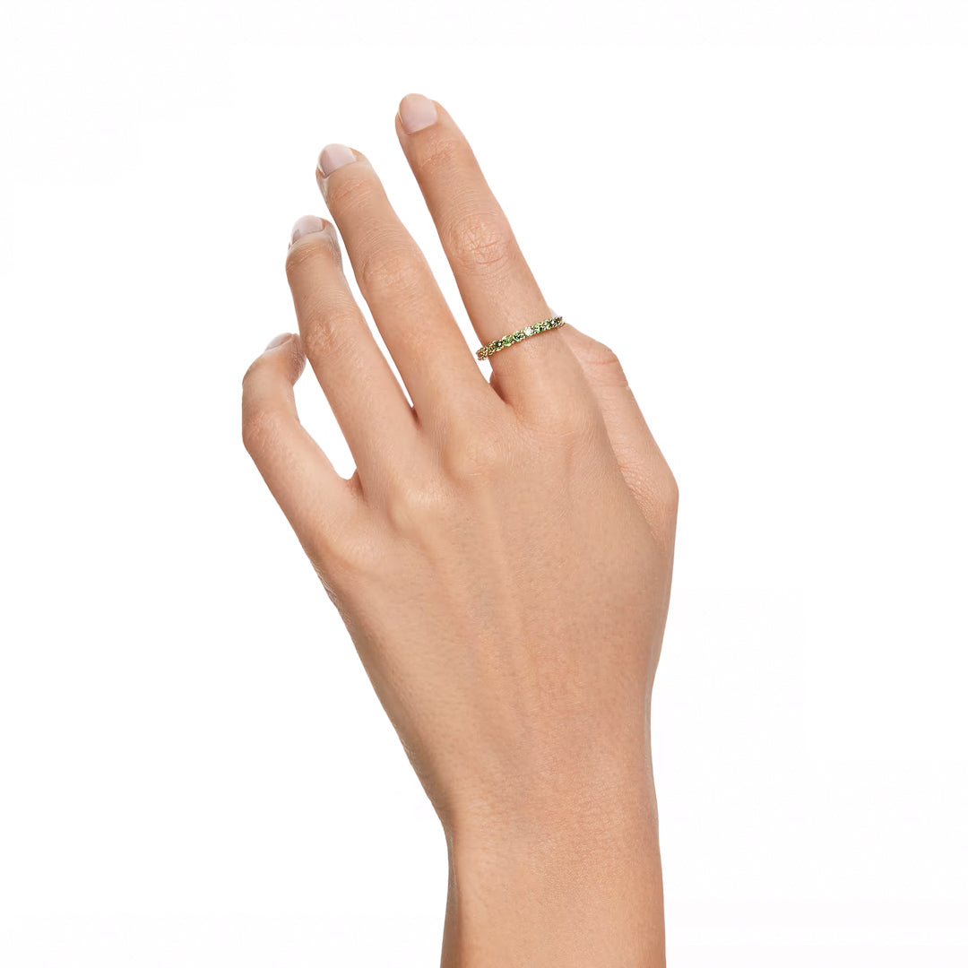 Against a plain white background, a hand with neatly trimmed nails showcases the Swarovski Matrix Ring—a delicate ring from the renowned brand Swarovski—featuring gold-tone plating and adorned with striking Matrix Vittore green stones on the ring finger.