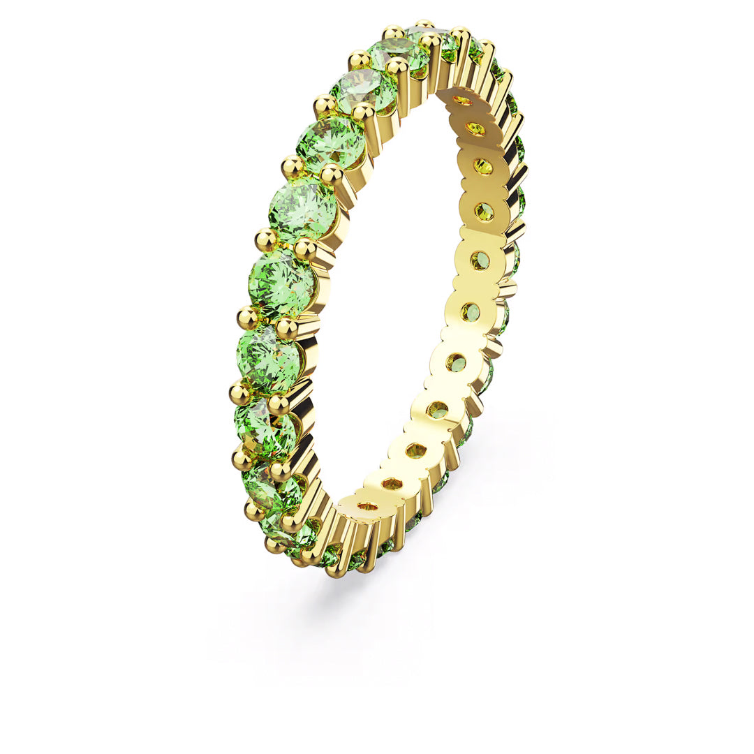 The Swarovski Matrix Ring by Swarovski, featuring a continuous row of small, round green stones, shines elegantly against a white background. Its vibrant hues and gold-tone plated finish make it an enchanting piece of jewelry.