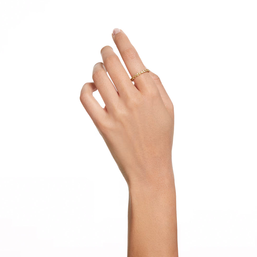 A hand with a light skin tone showcases the Swarovski Matrix Ring, featuring luminescent small beads delicately arranged. The fingers, gently bent against the plain white background, highlight the elegance of Swarovski's gold-tone plating.