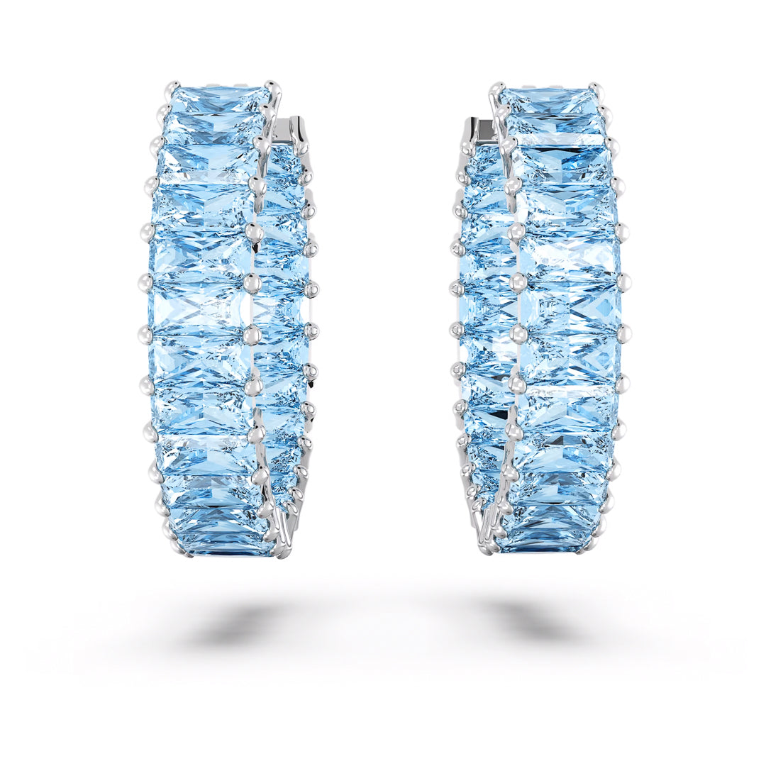 Close-up of Swarovski Matrix Hoop Earrings showcasing two silver hoops adorned with square-cut aquamarine stones, enhanced with rhodium plating for added shine. Set against a white background, the earrings appear suspended, with their shadows accentuating their elegant design.