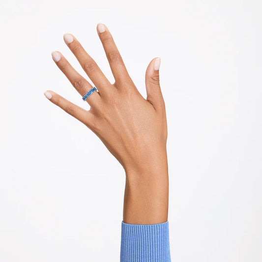 A hand adorned with the exquisite Swarovski Matrix Ring featuring an aquamarine gemstone is raised against a white background. The sleeve of a light blue sweater gracefully covers the wrist, enhancing the look of neatly manicured fingernails in a natural shade.
