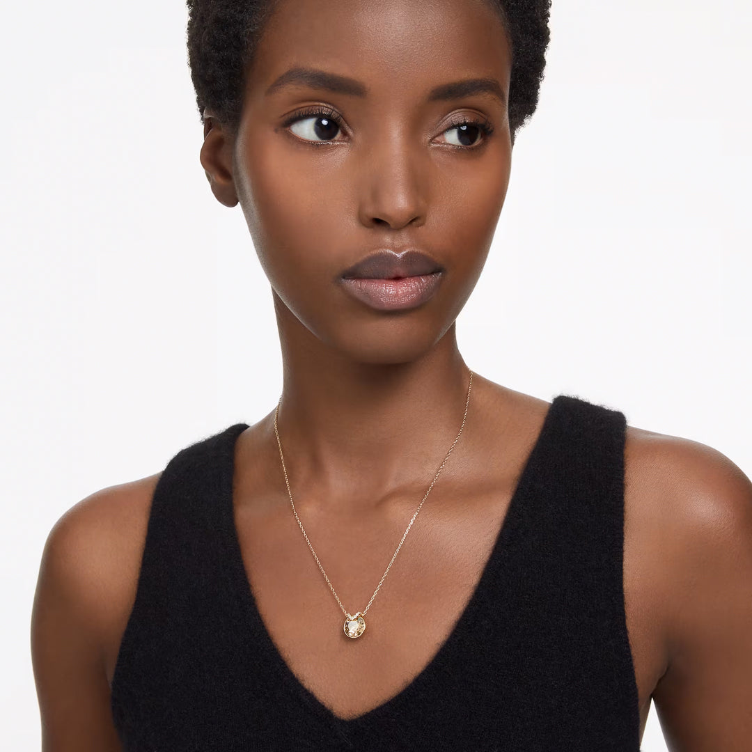 A person with short hair wearing a black sleeveless top gazes to the side, showcasing the Swarovski Bella V Necklace Pendant with its captivating center stone. The background is plain white.