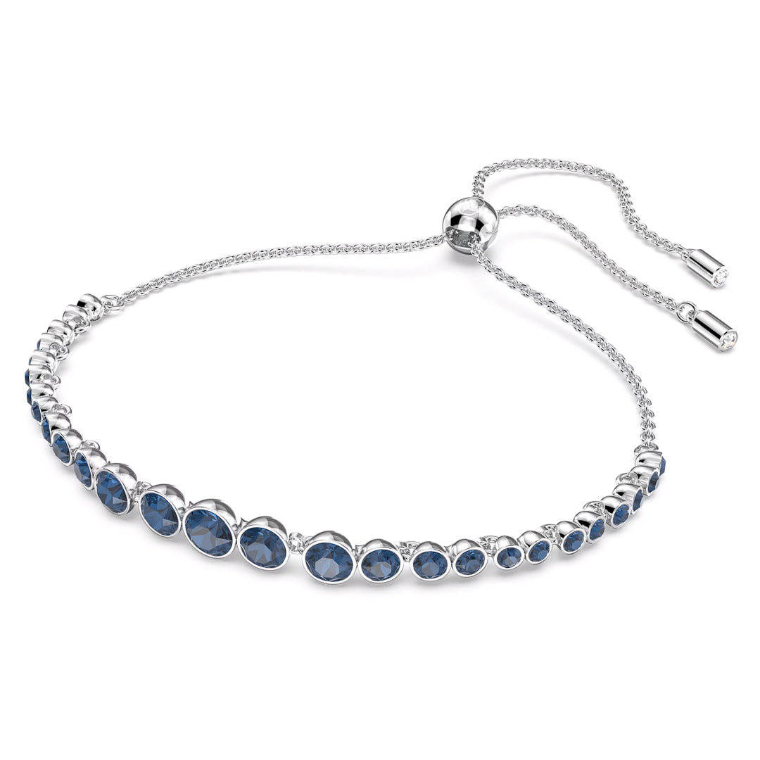 Introducing the elegant Swarovski Imber Emily Bracelet, a stunning piece by Swarovski. This rhodium-plated silver bracelet features a delicate adjustable chain and clasp, adorned with a row of round blue crystals beautifully set along its length.