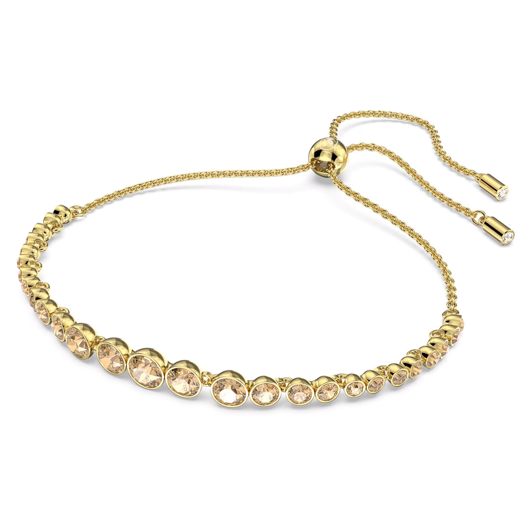 The Swarovski Imber Emily Bracelet by Swarovski showcases a gold-tone design with a series of round, light yellow gemstones set in individual bezels. It features an adjustable sliding clasp with two dangling ends, each embellished with a small golden crystal.