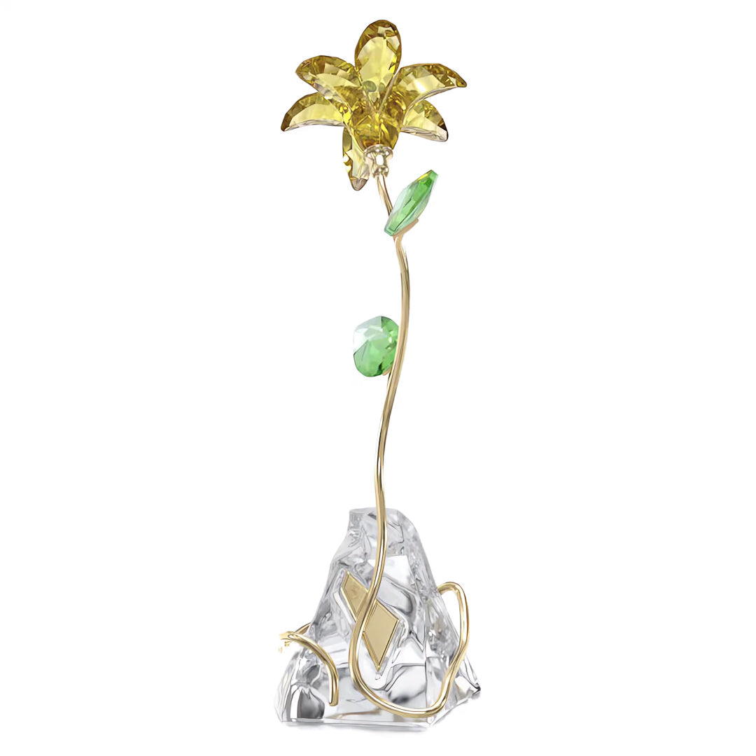 Introducing the Swarovski Florere Lily Home Décor by Swarovski: a stunning crystal sculpture showcasing a delicate yellow lily with an elegant, slender gold stem and two vibrant green leaves, all beautifully arranged on a clear, faceted base. Ideal for adding a touch of elegance to your home décor.