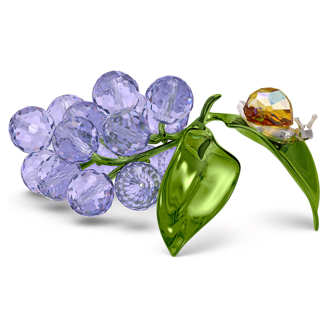 From the Swarovski Idyllia collection, the Swarovski Idyllia Snail and Blueberries Home Décor piece showcases a charming crystal snail perched among a cluster of blue and green crystal leaves, adding whimsy to the exquisite design.