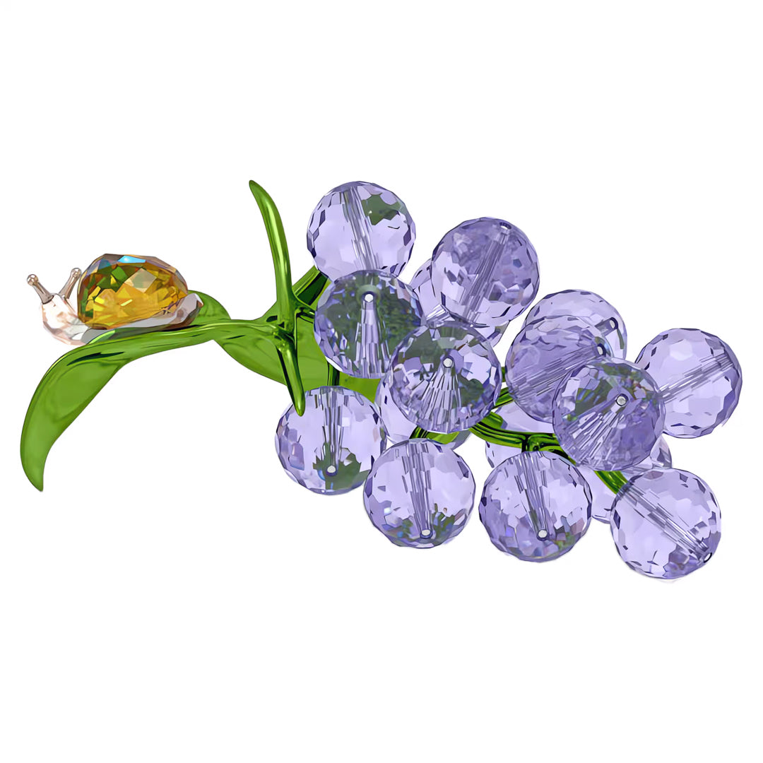 A stunning arrangement of sparkling purple blueberries with green leaves, crafted in a crystalline style reminiscent of the Swarovski Idyllia Snail and Blueberries Home Décor. A small, faceted snail with a yellow shell sits atop one of the leaves, against an elegant white background from the Swarovski collection.