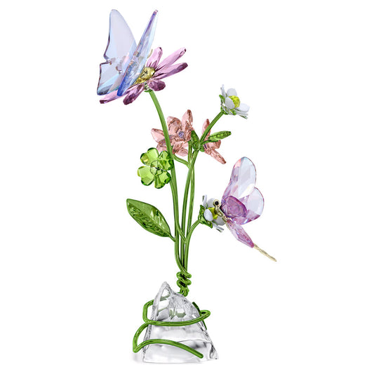 The Swarovski Idyllia Butterfly and Flowers Home Décor piece features a delicate butterfly resting atop pink and purple flowers with green leaves, all beautifully set on a clear, angular crystal base. This artwork from Swarovski embodies both elegance and vibrancy, capturing the whimsical charm of nature, making it an ideal addition to home décor.