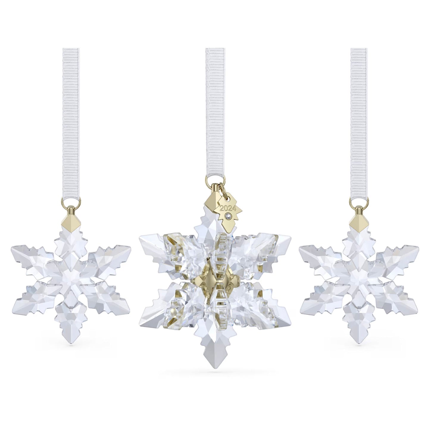 Three crystal snowflake ornaments hang from white ribbons, with the center one being a larger piece from the Swarovski Annual Edition 3D Ornament Set 2024. This middle ornament is adorned with a small gold tag inscribed "2024." Each ornament in the set sparkles with intricate facets, reflecting light beautifully and adding to the festive atmosphere.