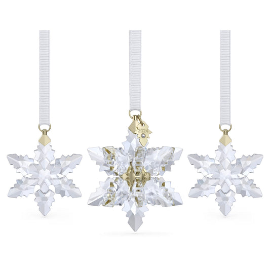 Three crystal snowflake ornaments hang from white ribbons, with the center one being a larger piece from the Swarovski Annual Edition 3D Ornament Set 2024. This middle ornament is adorned with a small gold tag inscribed "2024." Each ornament in the set sparkles with intricate facets, reflecting light beautifully and adding to the festive atmosphere.
