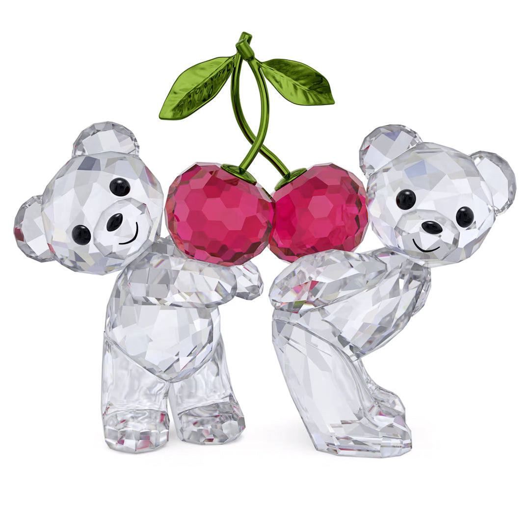 The Swarovski Kris Bear Always Together Home Décor figurine features two enchanting crystal teddy bears from the Kris Bear collection. They hold vibrant red crystal cherries adorned with green leaves, while the bears' clear, faceted design beautifully reflects light, highlighting their cheerful expressions against a simple white backdrop.