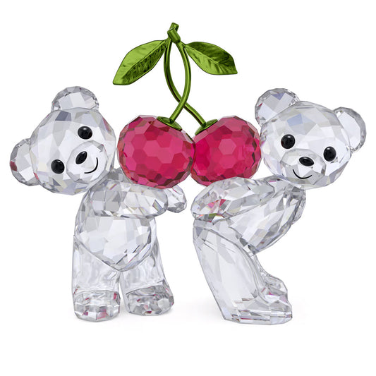 The Swarovski Kris Bear Always Together Home Décor figurine features two enchanting crystal teddy bears from the Kris Bear collection. They hold vibrant red crystal cherries adorned with green leaves, while the bears' clear, faceted design beautifully reflects light, highlighting their cheerful expressions against a simple white backdrop.