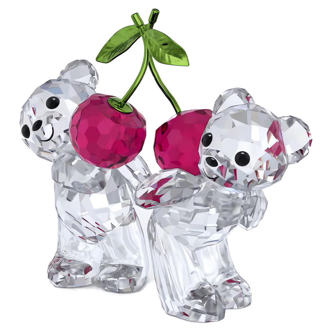The Swarovski Kris Bear Always Together Home Décor features two charming Kris Bear crystal figurines with faceted surfaces, playfully holding a pair of red crystal cherries embellished with green crystal leaves.