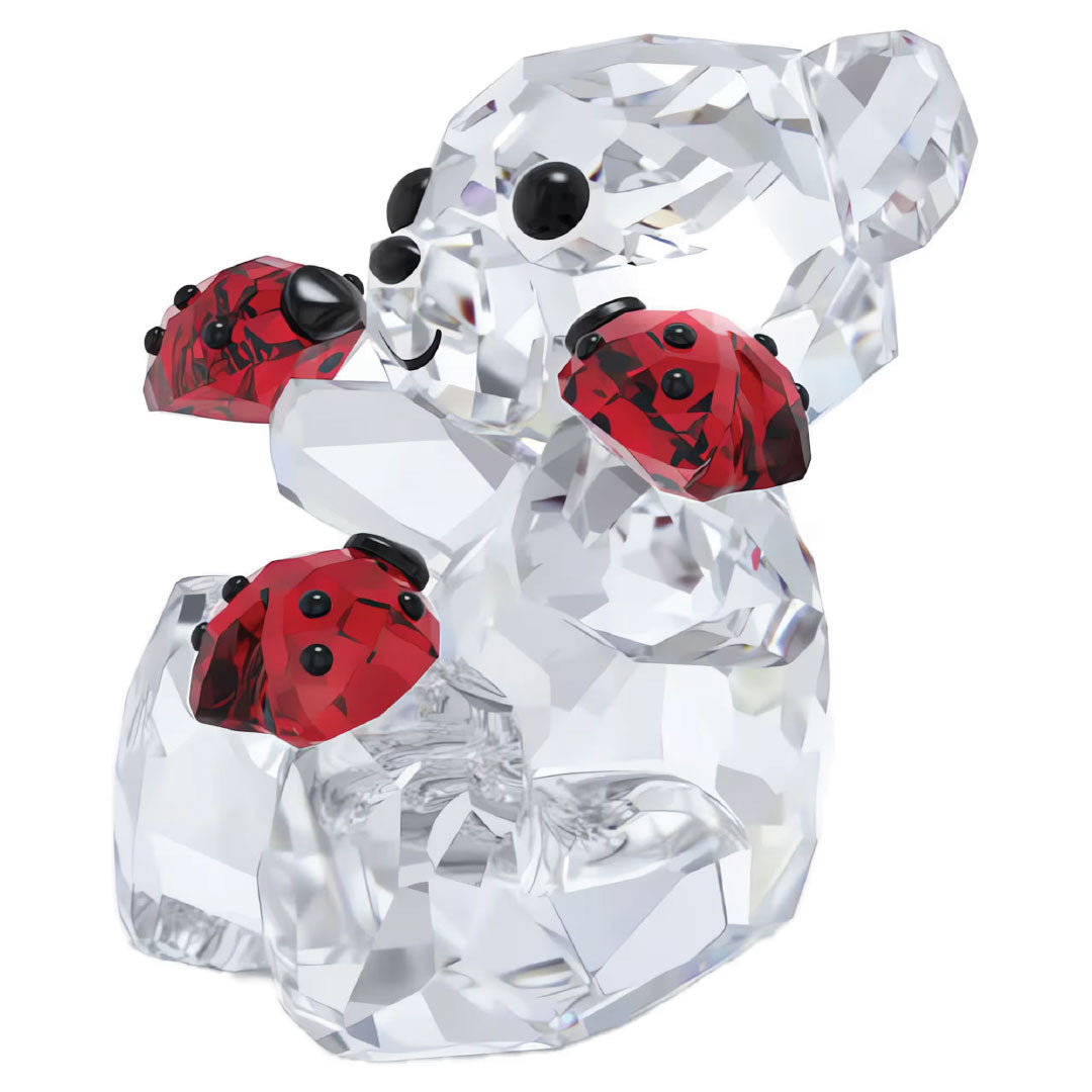 The Swarovski Kris Bear Good Luck Bear Home Décor features a charming crystal sculpture of a Kris Bear delicately embracing three red ladybugs, with their striking black-spotted bodies beautifully contrasting against the bear's clear, sparkling crystals.