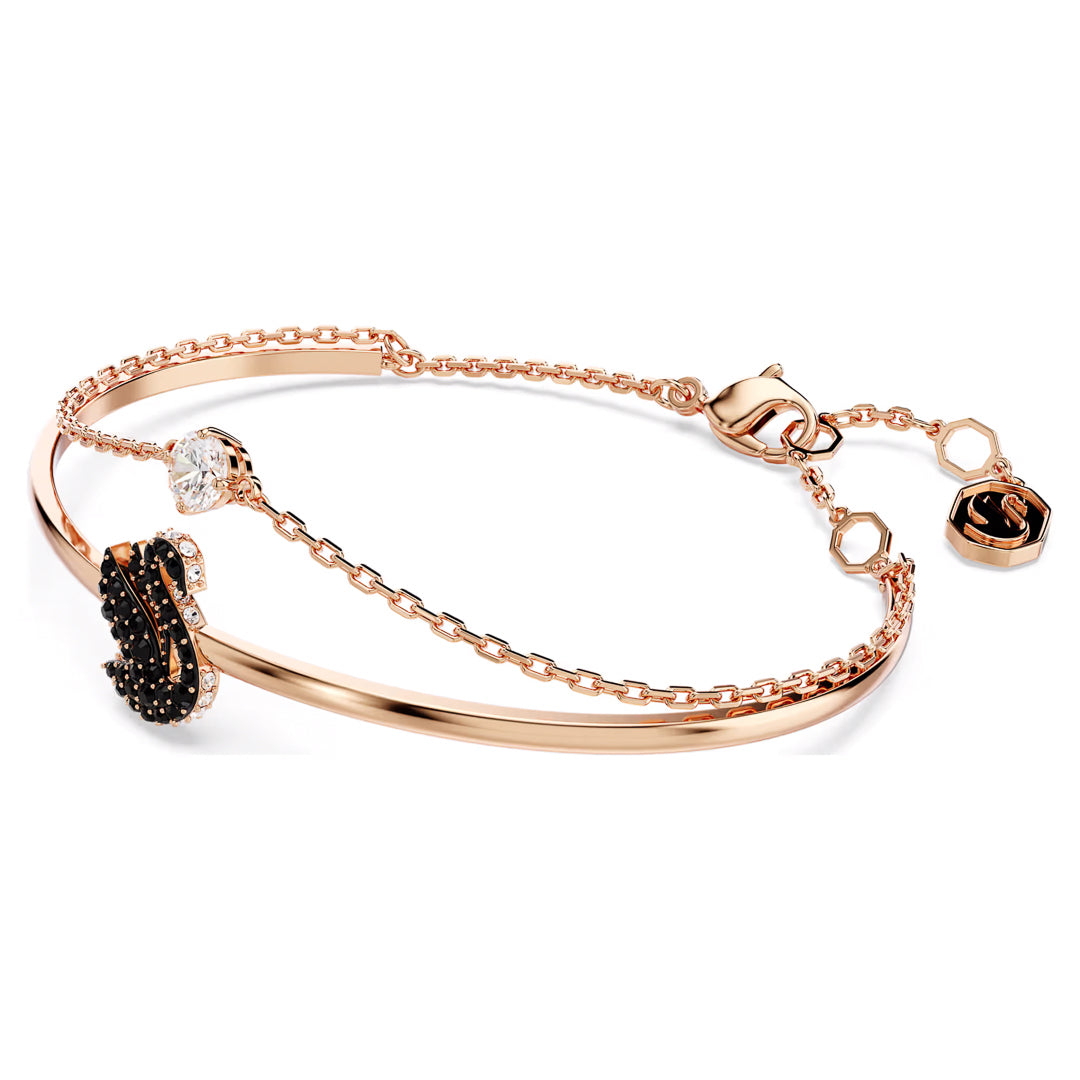 Introducing the Swarovski Swan Bangle by the renowned brand Swarovski: a delicate rose gold-tone bracelet showcasing a sleek bangle design with an elegant section of small chain links. It features a stunning black decorative accent, an eye-catching Swarovski crystal, and is finished with a secure lobster clasp closure.