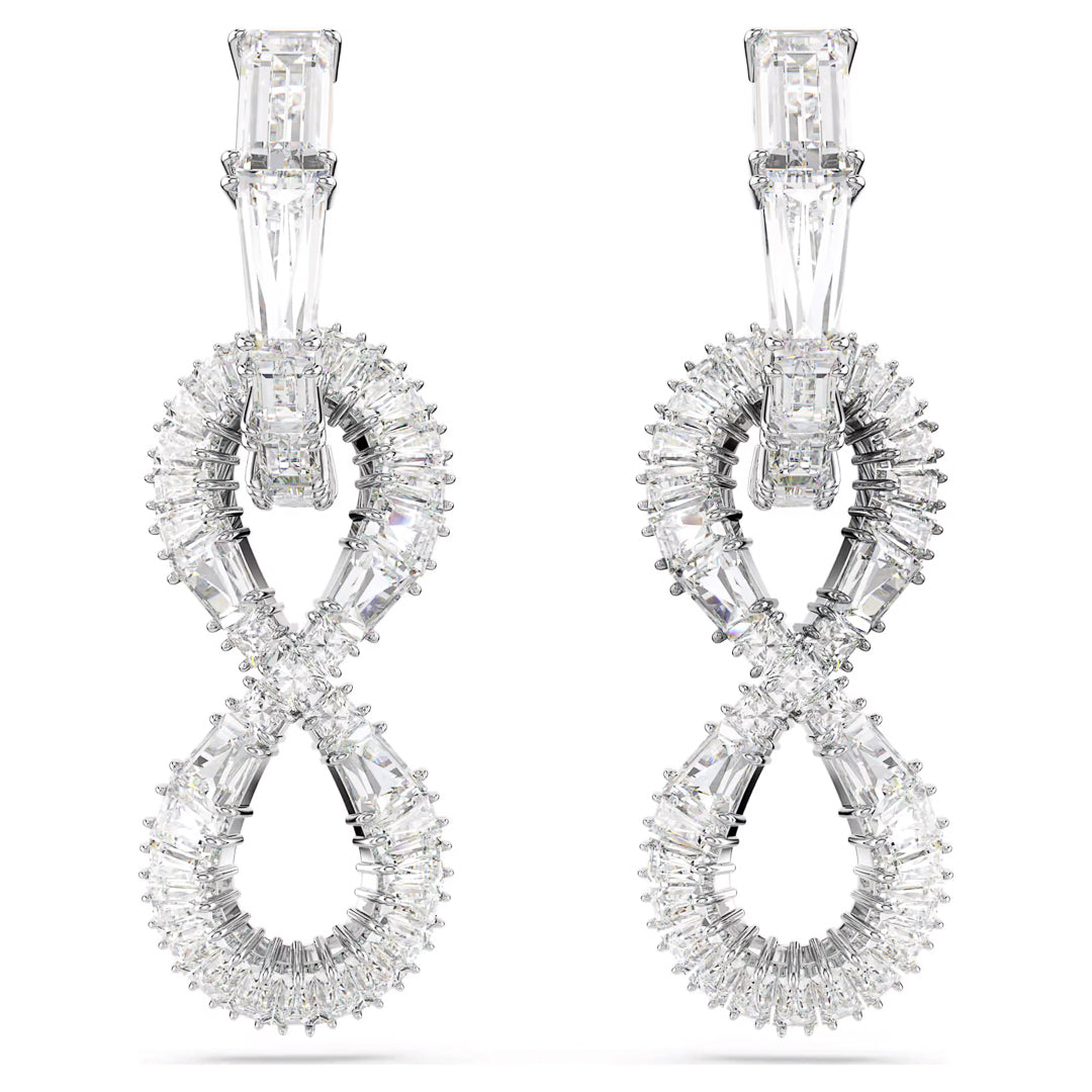 The Swarovski Hyperbola Drop Earrings feature a sophisticated rhodium-plated finish with an intricate figure-eight design. These earrings are adorned with sparkling diamonds and rectangular gemstones at the top, creating a luxurious and refined appearance synonymous with Swarovski's elegance.