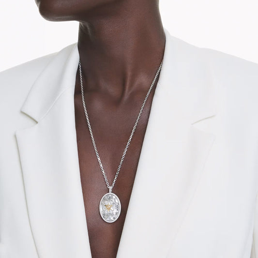 A person wearing a white blazer is shown from the neck down, accentuating the Swarovski Idyllia Necklace Pendant. This rhodium-plated piece features a central gemstone and boasts an elegant floral design from the renowned Swarovski jewelry collection. The background is plain white.