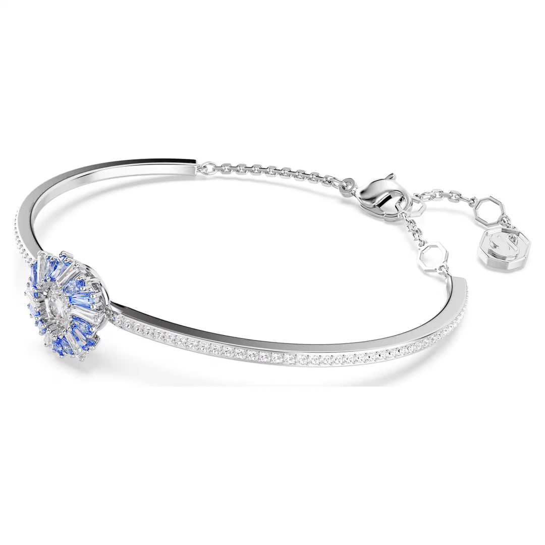 Presenting the Swarovski Idyllia Bangle, a stunning rhodium-plated silver bracelet that highlights a central round floral design adorned with delicate blue and clear Swarovski Zirconia gemstones. It is completed with an adjustable chain clasp to ensure an ideal fit.
