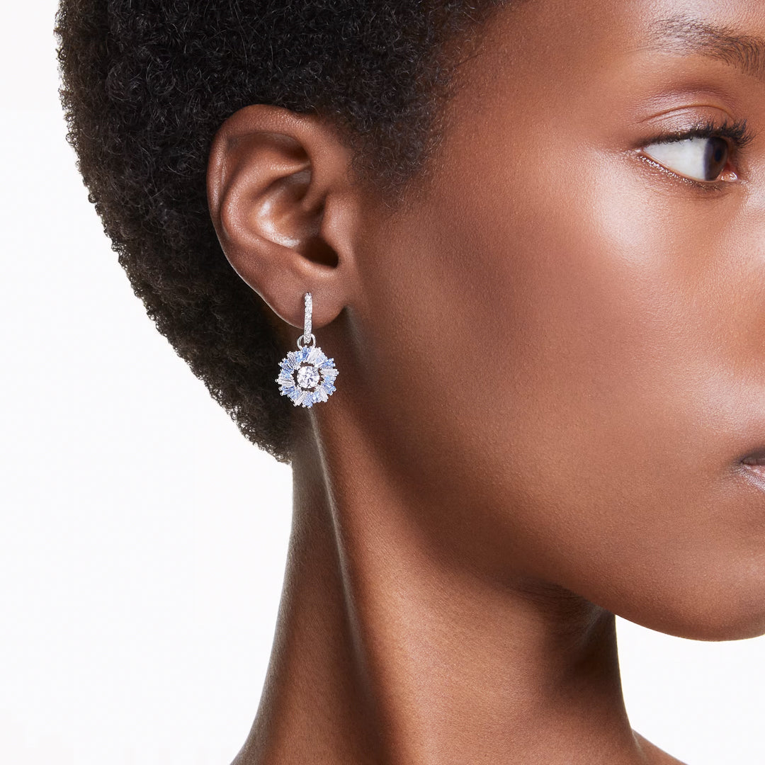 A close-up of a person with short hair showcasing a sparkling Swarovski Idyllia Drop Earring. This elegant piece of jewelry from Swarovski features a central zirconia stone surrounded by smaller gems, set against a neutral background.