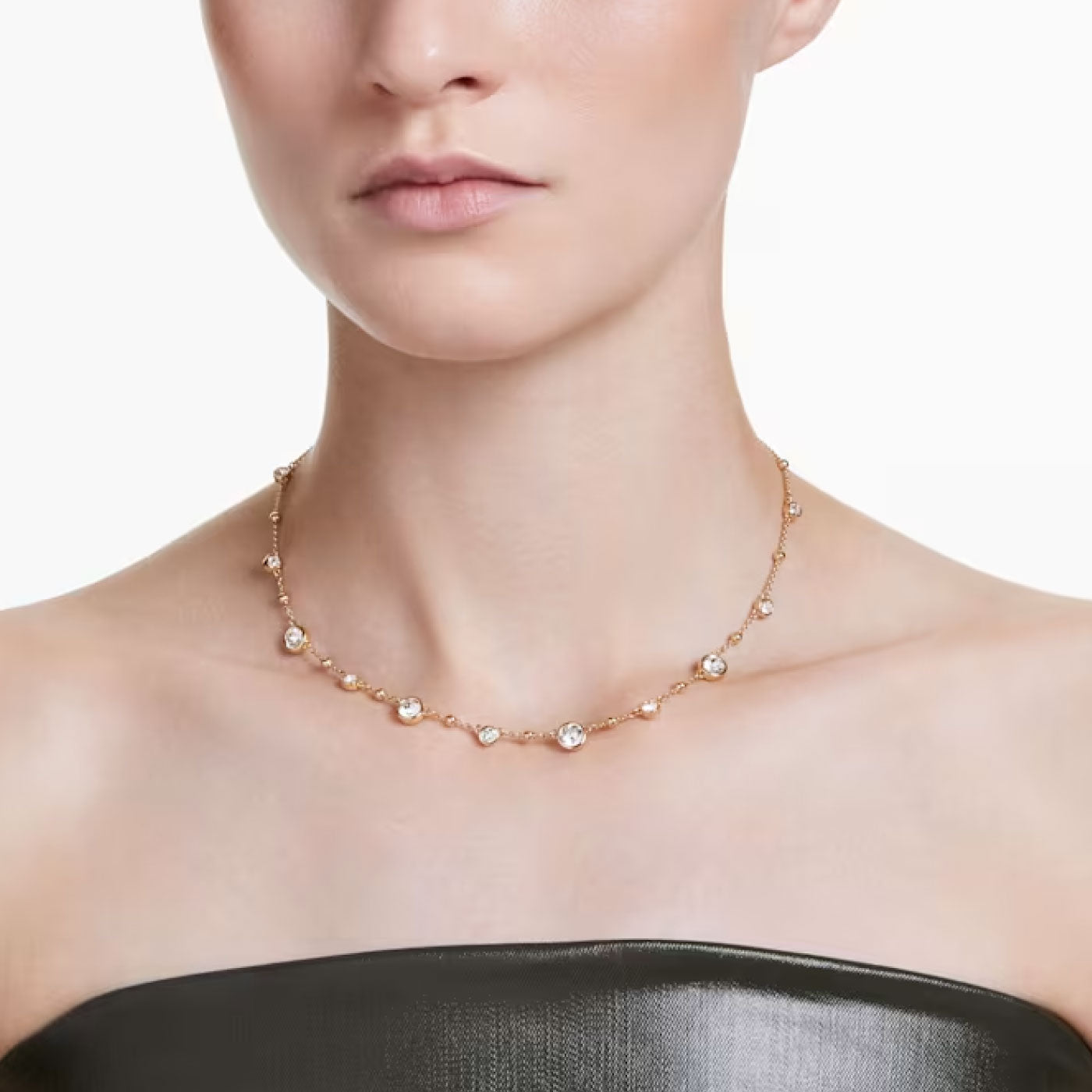A person wearing the Swarovski Imber Station Necklace, featuring evenly spaced pearls and dazzling Swarovski Zirconia, paired with a strapless dark green top against a plain white background.