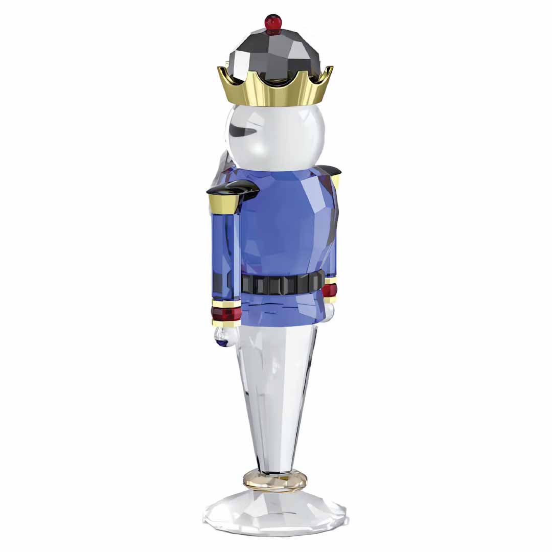 The Swarovski Holiday Cheers Blue Nutcracker Home Décor piece features a crystallized nutcracker soldier with a golden crown and a blue and gold uniform, standing elegantly on a clear base, making it an ideal addition to your holiday decor.