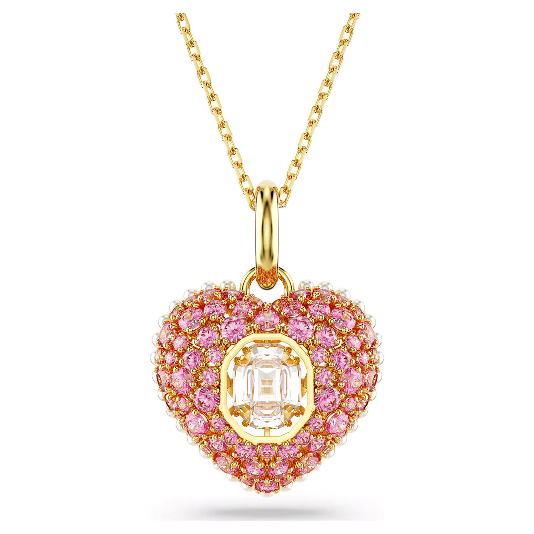 Introducing the Swarovski Idyllia Necklace Pendant, a stunning piece from Swarovski. This exquisite gold necklace features a delicate chain and an intricate heart-shaped pendant adorned with pink Swarovski Zirconia. At its center is a larger, transparent rectangular gemstone that enhances the overall elegance of the design.