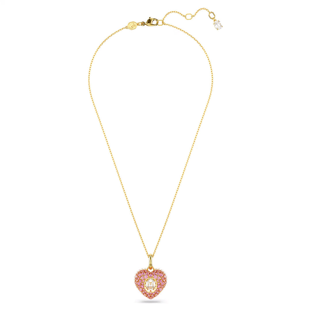 The Swarovski Idyllia Necklace Pendant by Swarovski is a delicate gold-tone plated piece featuring a heart-shaped pendant adorned with pink Swarovski Zirconia and a central clear gemstone. The chain includes an adjustable clasp and a small charm.